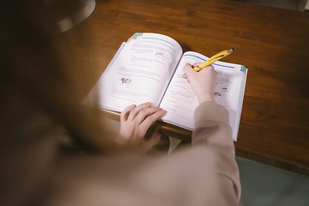 Henkilö kirjoittaa kynällä avoimeen tehtäväkirjaan